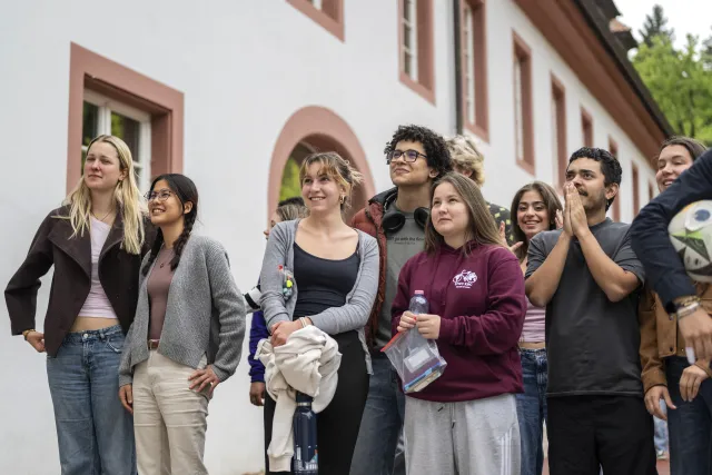 Schülerinnen und Schüler stehen vor dem Schulgebäude und klatschen in die Hände, um Prüflinge anzufeuern.