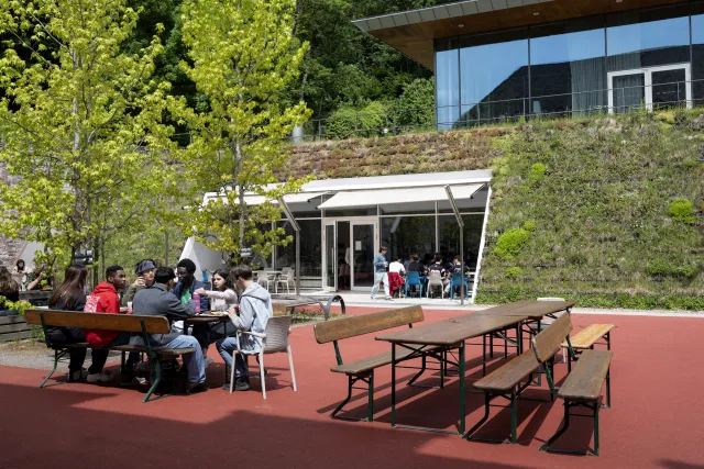 Der Schulhof des UWC in Freiburg. Auf dem Platz stehen Tische und Bänke, an einigen sitzen Schüler:innen und essen. 